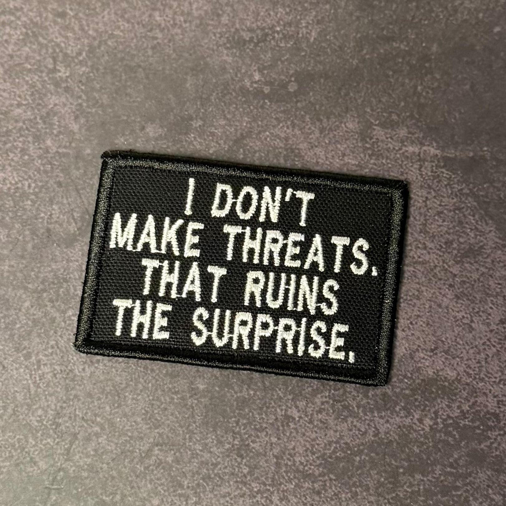I Don't Make Threats, That Ruins The Surprise Funny Morale Patch, 2x3" | Made in USA | VELCRO® Brand Hook Backing